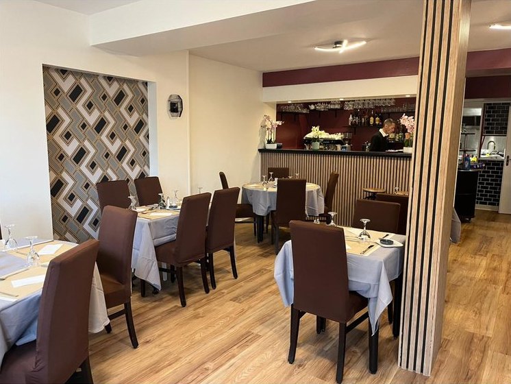 La salle du restaurant : tables dressées, fauteuils bruns et mur bordeaux